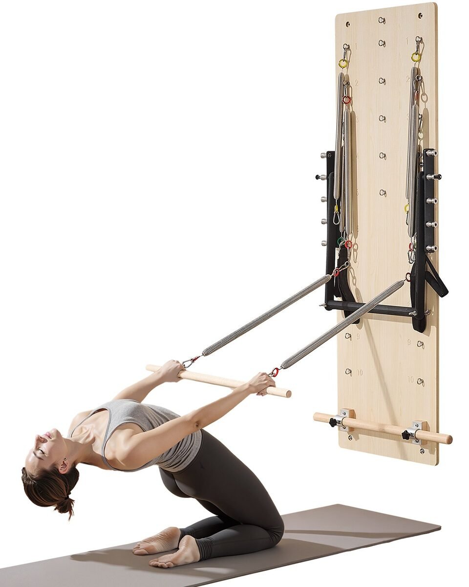 Žena na prostirci vježba s drvenim štapom spojenim oprugama na zidnu pilates ploču